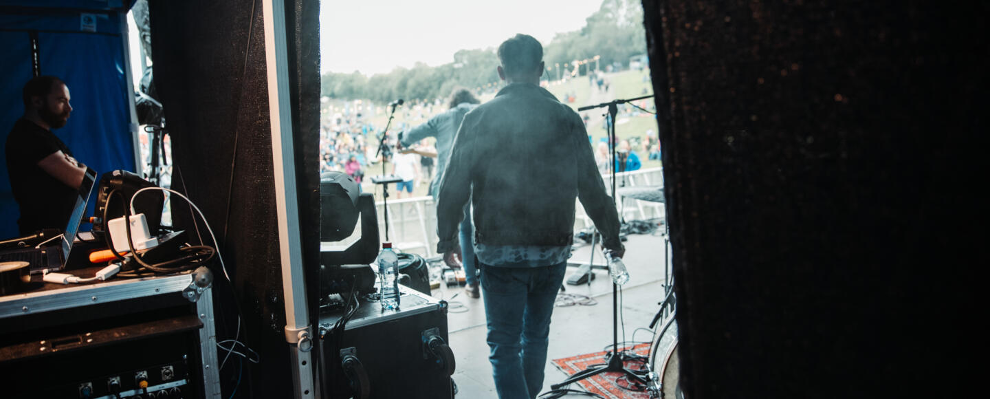 Two members are walking out onto a stage in front of a large outdoor audience