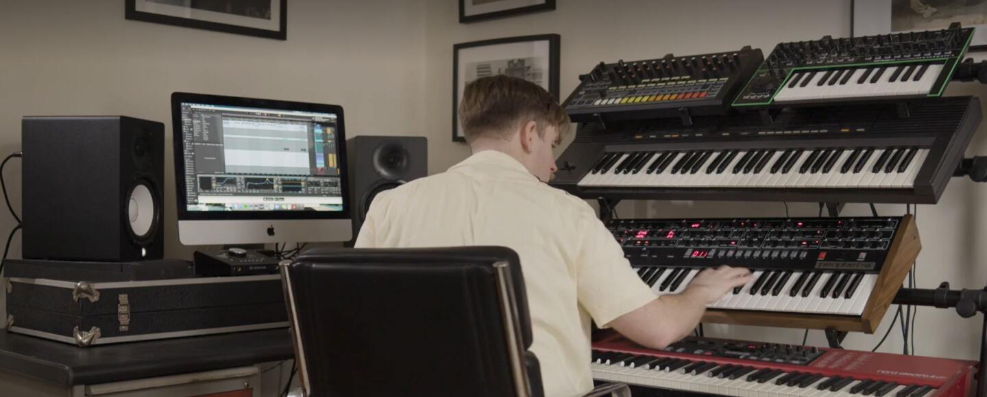 Tom from Rhumba Club sat facing away from the camera playing on a stack of keyboards on his desk