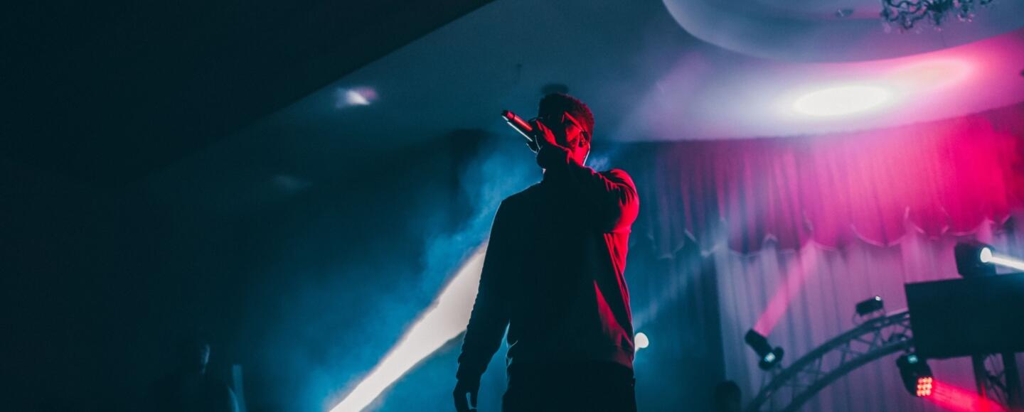 A singer performing on a dark stage in front of coloured lights