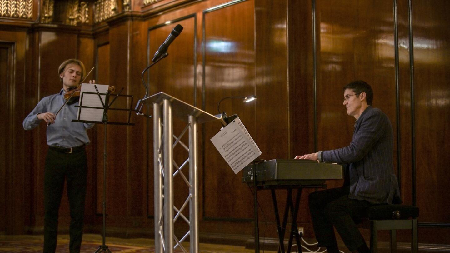 A violinist and a pianist play their instruments in a small room