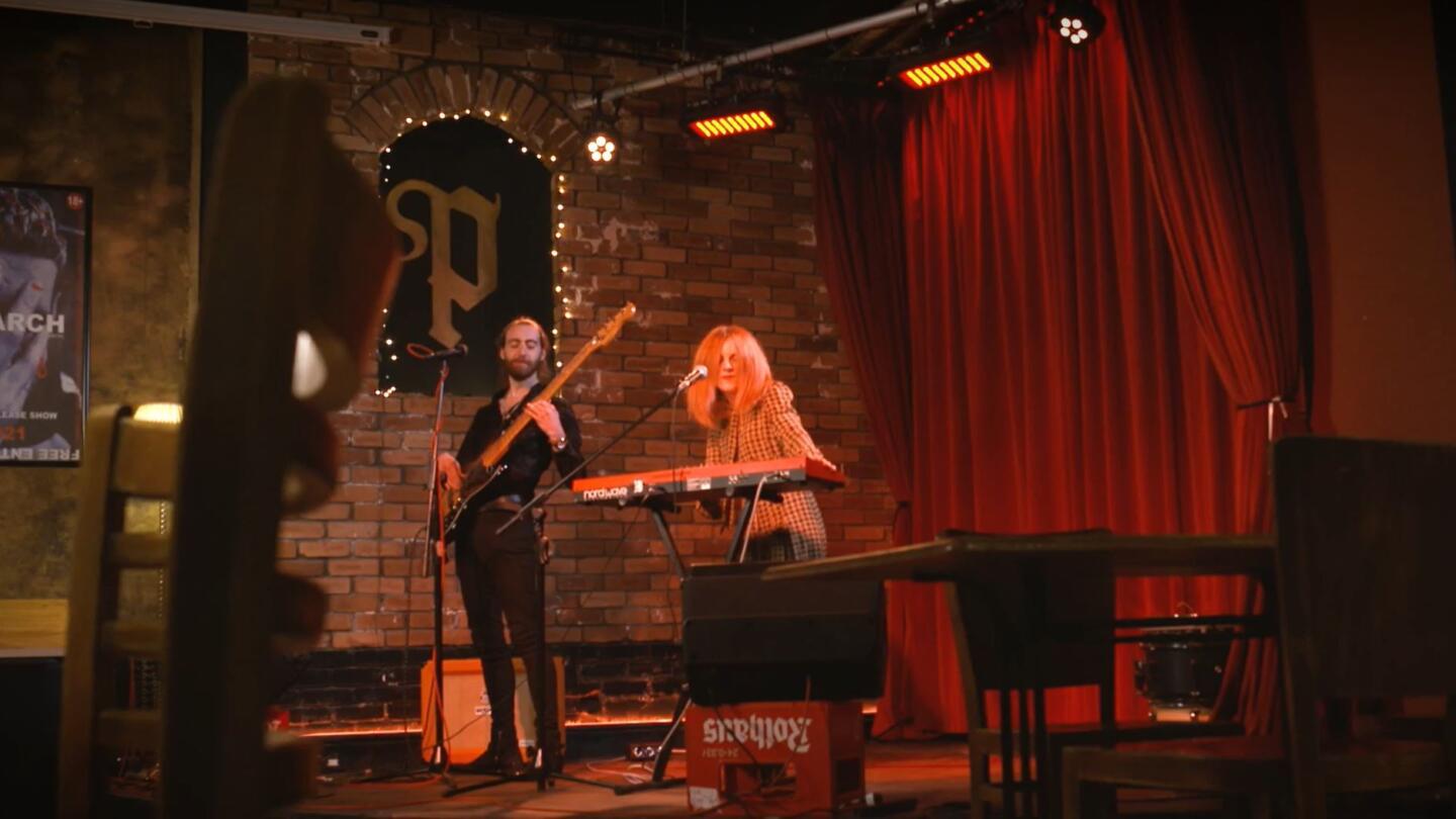 A man on stage playing bass while a woman next to stands behind a keyboard and sings