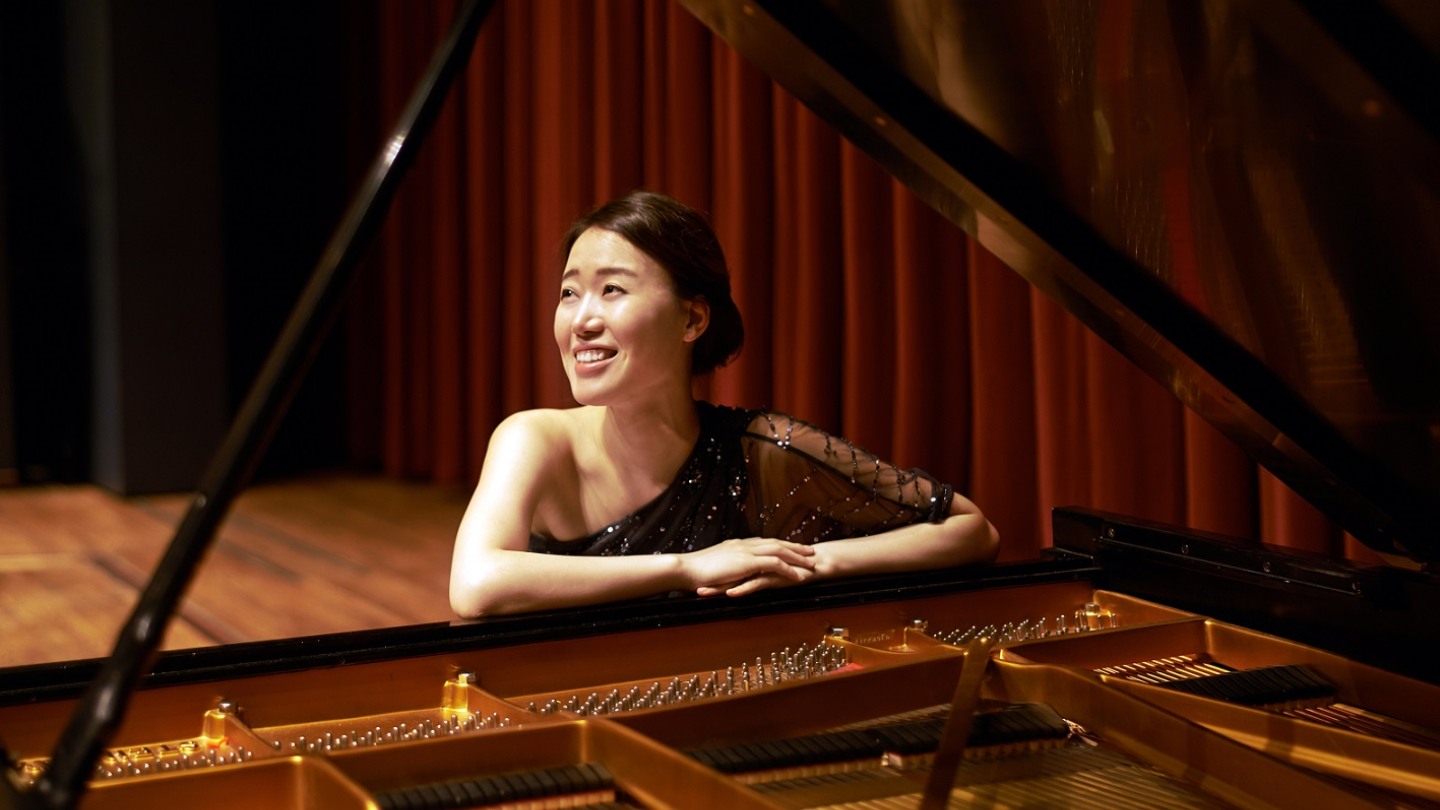 A pianist sits at a piano, smiling and looking into the distance