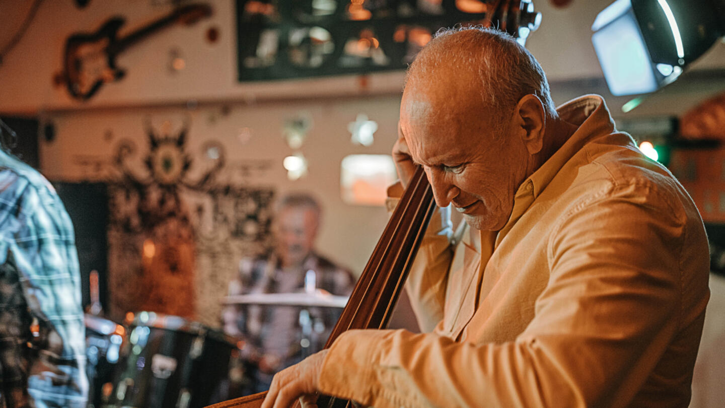 Elderly musicians playing together, with a man in the foreground performing on a cello