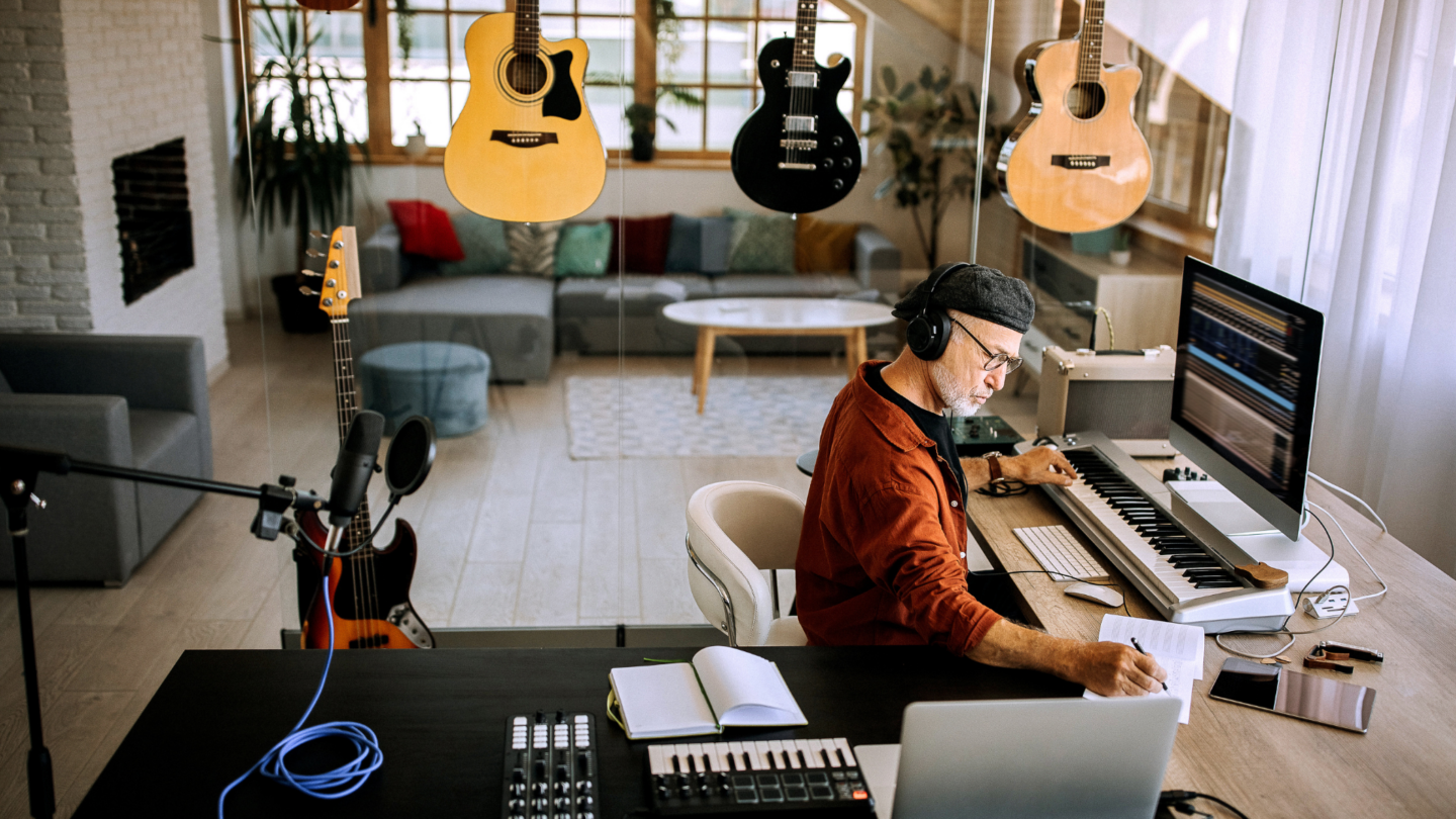 Musician working on a laptop in an open‑plan music studio, writing songs and surrounded by guitars and instruments