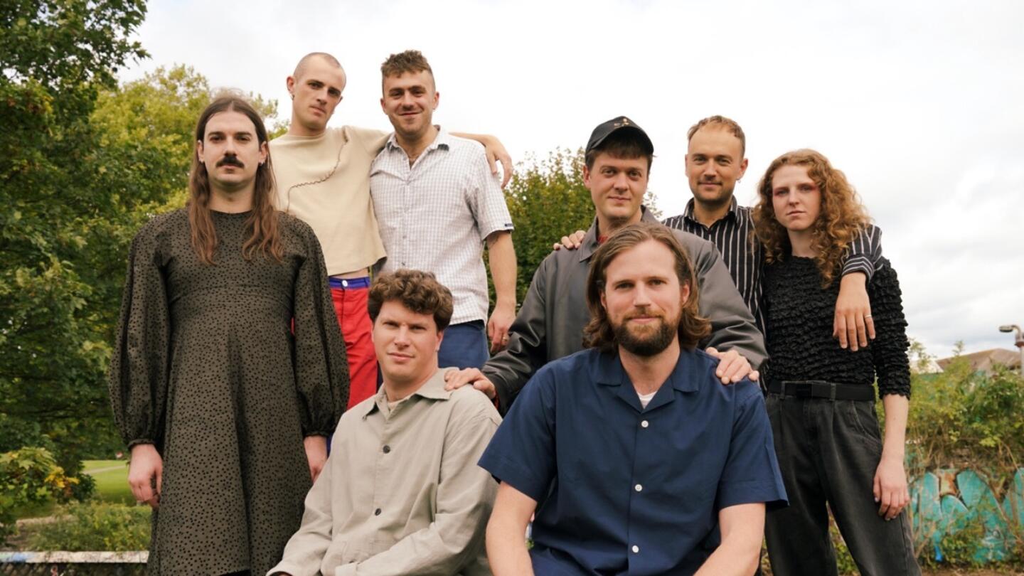 8 piece band caroline stand together outside surrounded by greenery