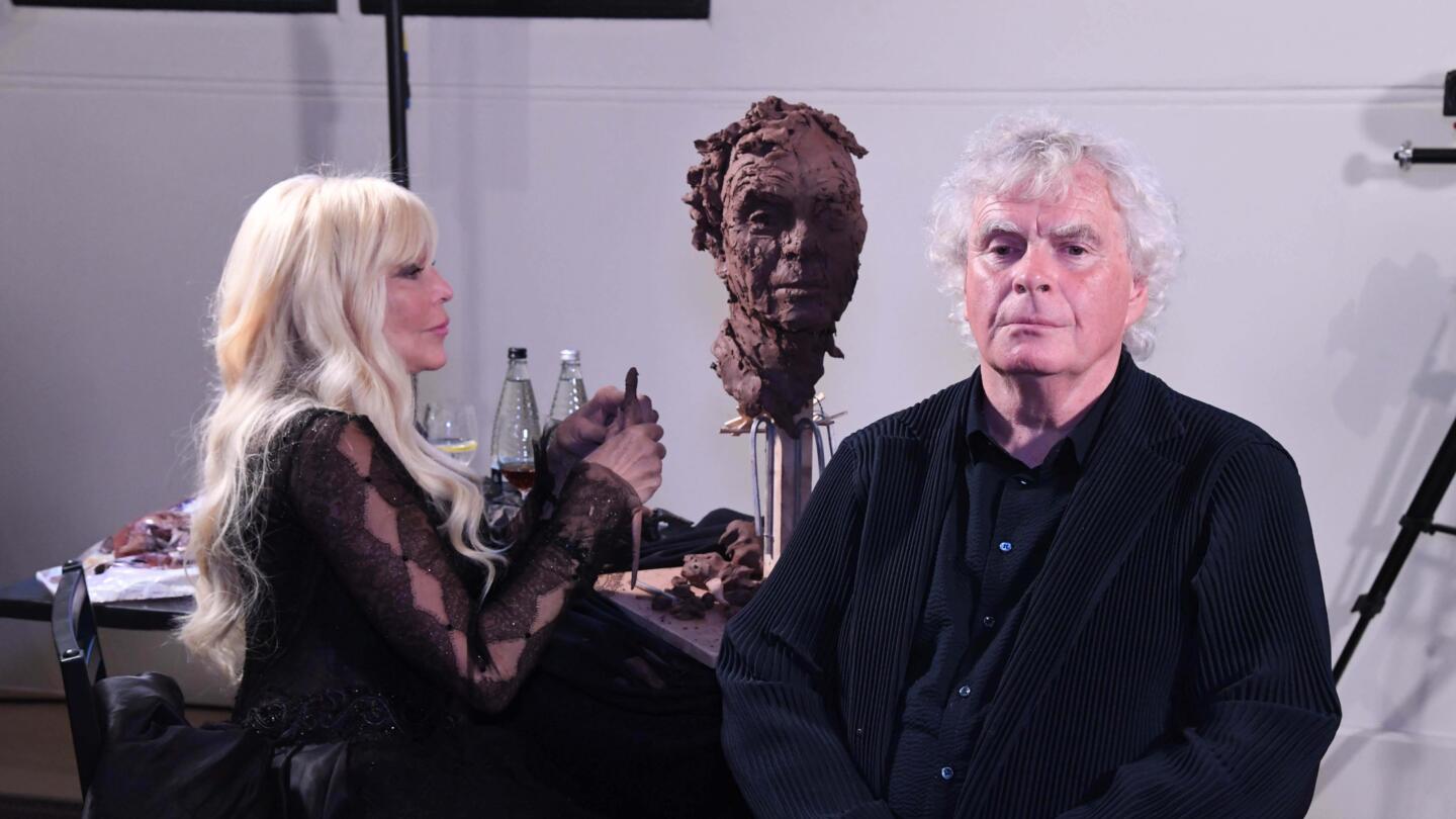 Simon Rattle sits for a sculptor while she sculpts his likeness