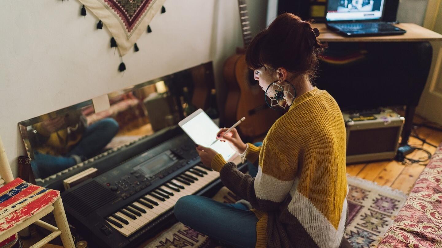 A musician composing music at their keyboard. They are sitting on the floor.