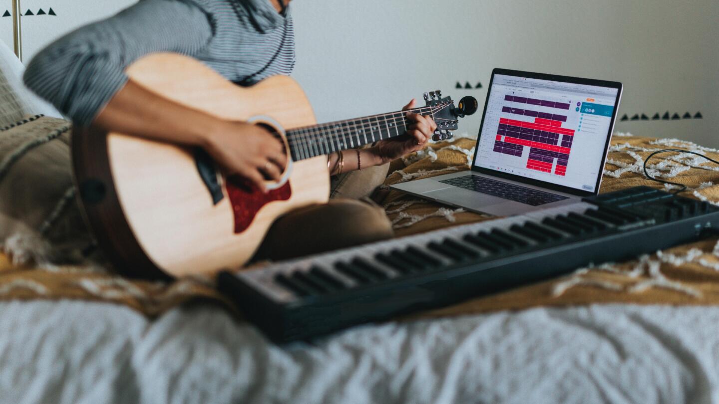 Musician recording themselves playing the keyboard and guitar on their bed
