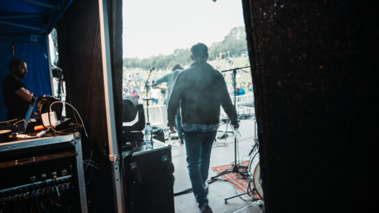 Two members are walking out onto a stage in front of a large outdoor audience