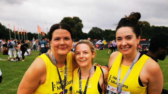 Three ladies in Help Musicians vests smile at the camera. They are wearing medals suggesting they've just completed a race.