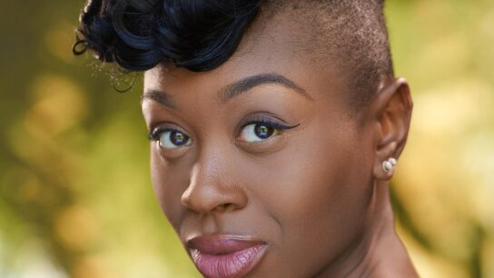 Close up headshot of Miriam-Teak Lee with greenery in the background
