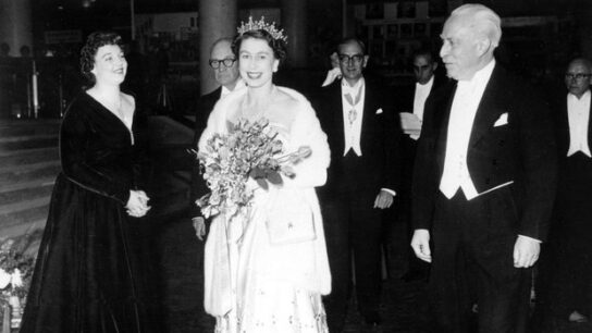 Queen Elizabeth arriving at the Royal Festival Hall holding a bouquet of flowers next to Sir Arthur Bliss