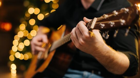 A musician playing a guitar with fairylights in the background