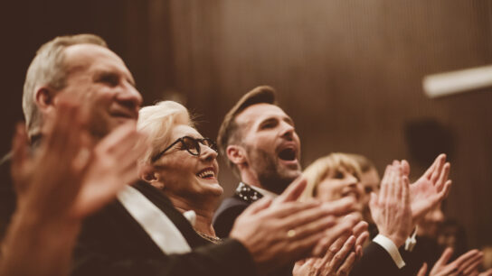 A concert audience smiles and applauds enthusiastically