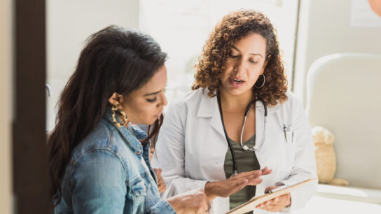 A doctor wearing a stethoscope shows a female patient some notes