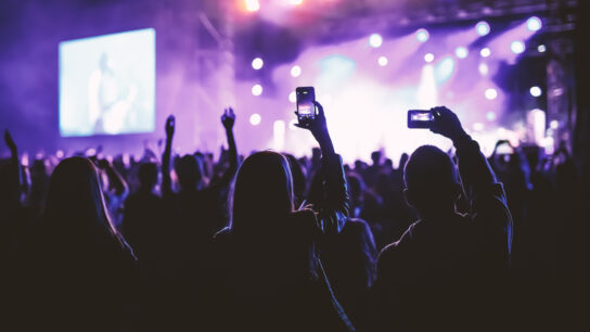 A large audience at a music concert. Some people are holding up smartphones to photograph the stage