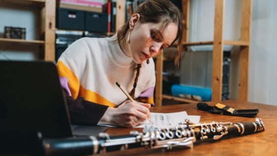 A musician sits writing music with a clarinet in front of her