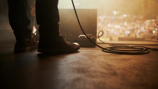 A musician's boots next to a microphone cable standing in front of an outdoor festival audience