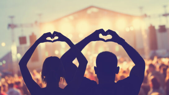 Two people making heart shapes with their hands at an outdoor gig