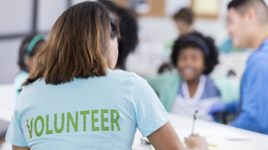 A girl in a volunteer t-shirt writes with a pen at a desk